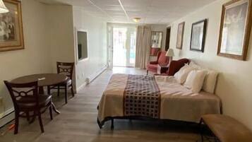A hotel room with a bed, a desk, and chairs. There is a hallway leading to another room.