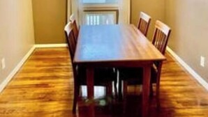 A dining room with a wooden table and chairs, a ceiling fan, and a window with curtains.