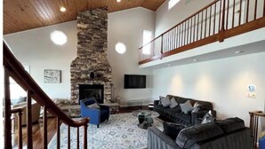 Un salón espacioso con chimenea de piedra, un sofá grande de color gris y una escalera de madera.