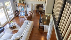 A spacious living room with a white sofa, a leather armchair, and a dining area with a round table and chairs.