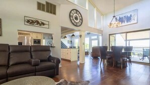 A spacious living area with a leather sofa, a round woven coffee table, and a rustic wood accent. A large clock and a framed artwork are on the walls.