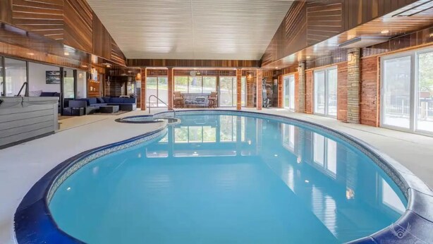 An indoor swimming pool with a curved design, wooden paneling on the walls, and a seating area with a table and chairs.