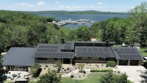 A modern house with solar panels on the roof, a large backyard, and a view of a lake with boats.