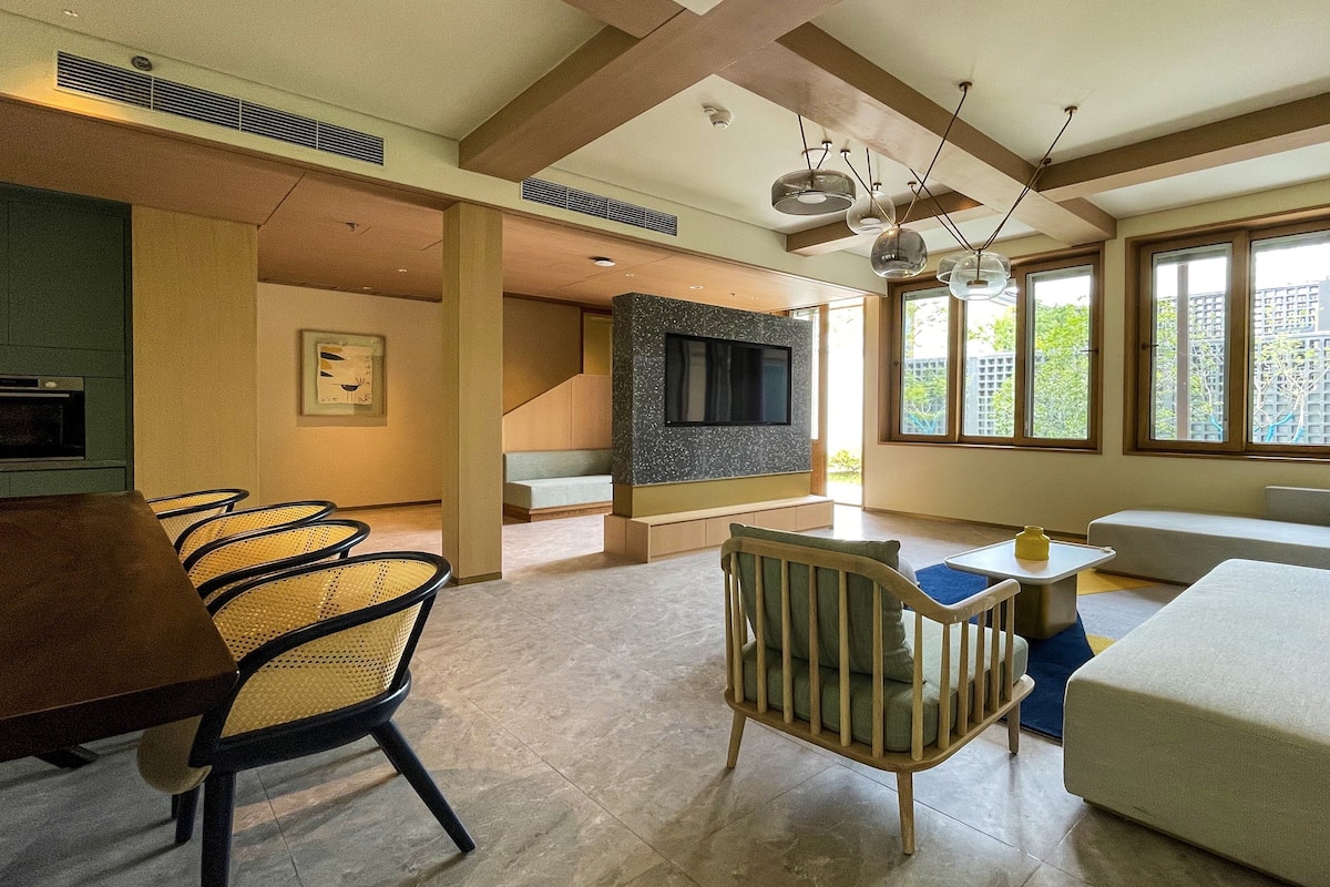 Un salon moderne comprenant un canapé, des fauteuils, une table à manger et un téléviseur fixé à un mur en pierre.
