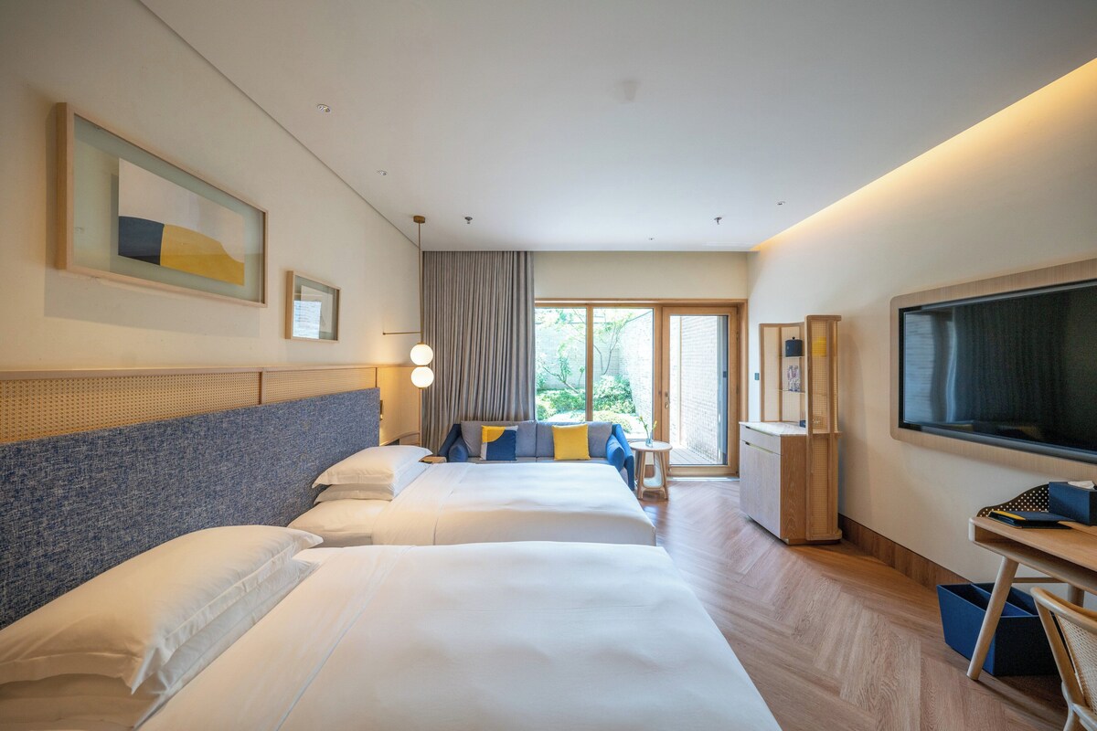 Une chambre d’hôtel avec deux lits, un bureau, une télévision et une vue sur l’extérieur.