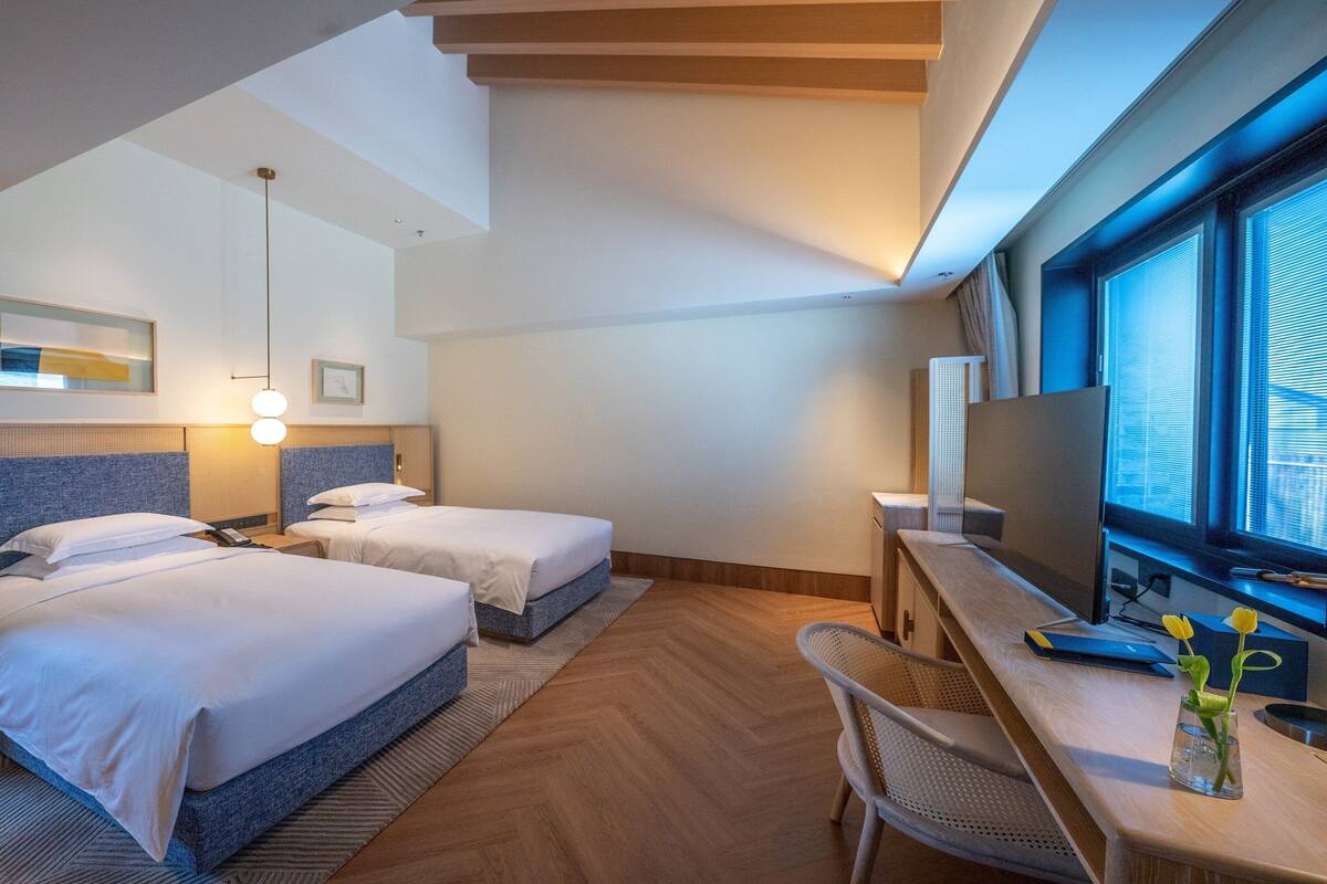 Une chambre d’hôtel avec deux lits, un bureau, une télévision et une grande fenêtre.