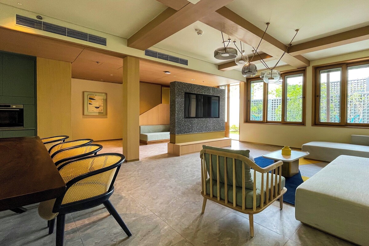 Un salon moderne comprenant un canapé, des fauteuils, une table à manger et un téléviseur fixé à un mur en pierre.