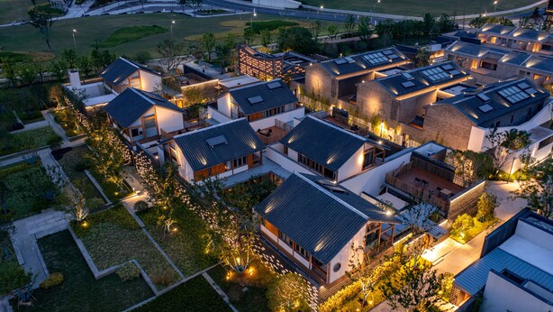 An aerial view of a modern residential area with multiple buildings, well-maintained lawns, and a curved road in the background.
