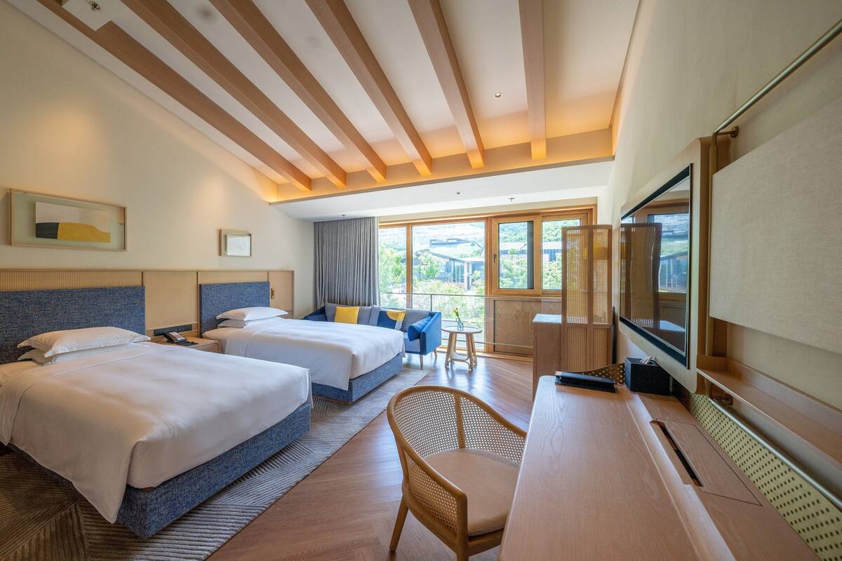 Une chambre d’hôtel avec deux lits, un bureau, une chaise, une télévision et un balcon avec vue.