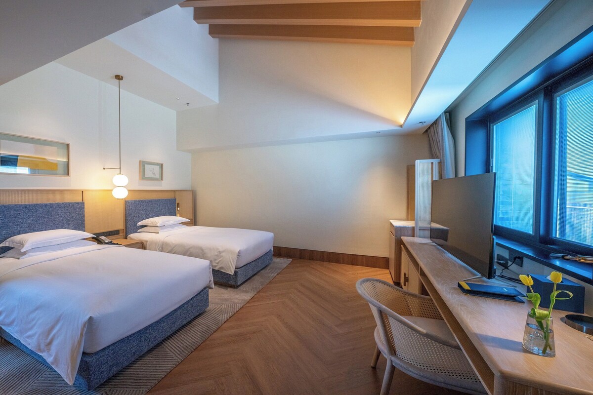 Une chambre d’hôtel avec deux lits, un bureau, une télévision et une grande fenêtre.