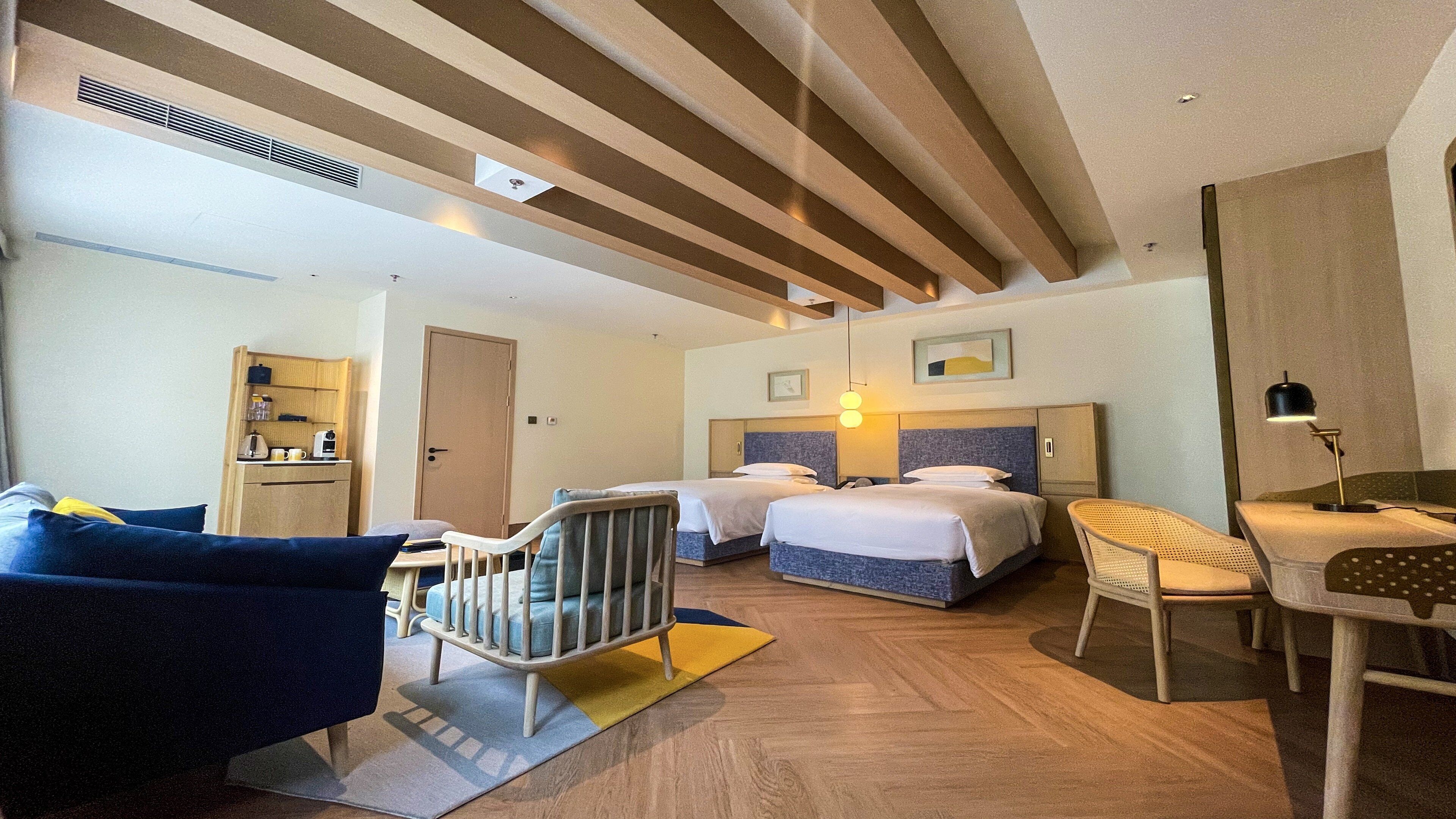 Habitación de hotel con dos camas, un escritorio, una silla, una cuna y una kitchenette.