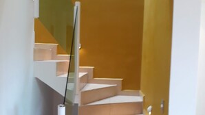 Uma escadaria moderna com corrimão de vidro, que leva a um patamar com parede amarela.
