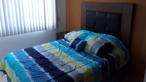Um quarto com uma cama, cabeceira, janela com persianas e uma parede.