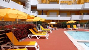 A poolside area with yellow sun loungers and umbrellas, surrounded by red flowers and a pool.