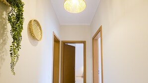 A hallway with a hanging plant, a textured wall decoration, and a potted plant on the floor.