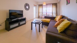 A living room with a TV, sofa, coffee table, and a dining area with a table and chairs.