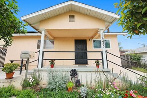 A two-story house with a beige exterior, a black front door, and a small porch with potted plants.