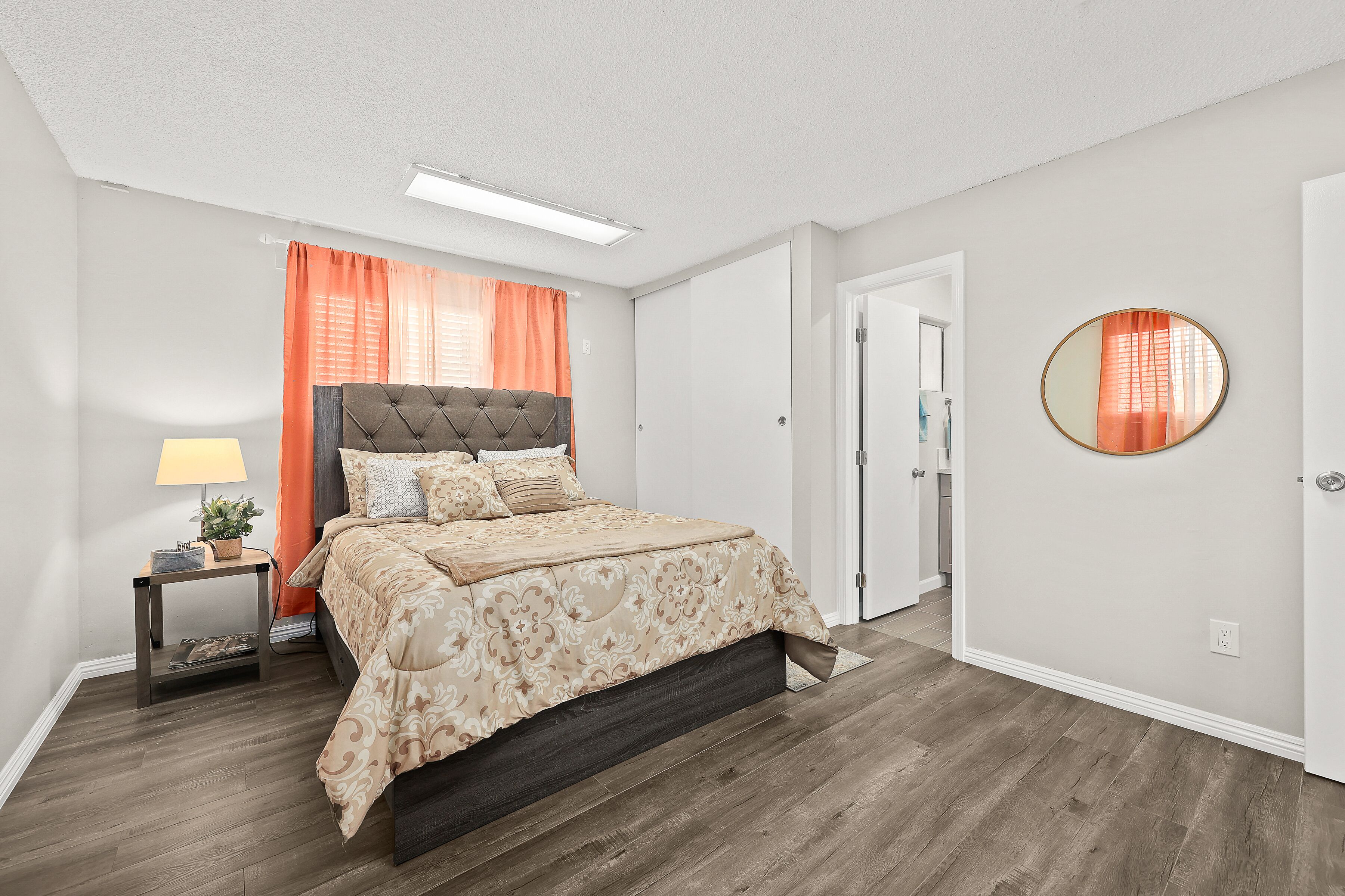 A bedroom with a bed, a nightstand, a lamp, a mirror, and a door.