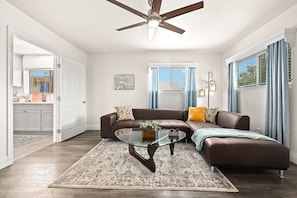 A modern living room with a sectional sofa, a glass coffee table, and a ceiling fan.