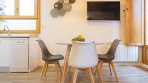 Una cocina moderna con una mesa de comedor, dos sillas, un televisor en la pared y un lavavajillas.