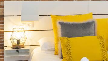 Una cama con ropa blanca y varias almohadas, incluyendo una amarilla y otra gris.