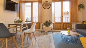Una sala de estar con una mesa de comedor, sillas, un sofá, un televisor y un reloj en la pared.