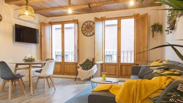 Una sala de estar con sofá, mesa de comedor, sillas, televisor y un reloj en la pared.