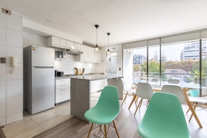 Una cocina moderna con armarios blancos, una isla integrada y un comedor con sillas verdes.