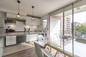 Una cocina moderna con una mesa de comedor de vidrio, armarios blancos y vistas a la ciudad a través de amplias ventanas.