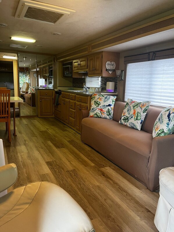 A compact RV interior with a kitchenette, a sofa with patterned pillows, and a dining area.