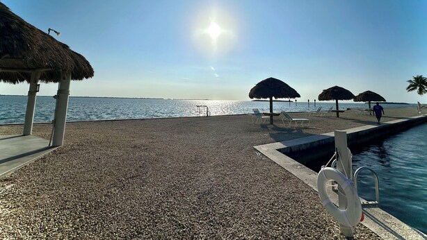 A beach with pebbled ground, thatched umbrellas, a lifebuoy, and a clear sky. - Relaxing  Home in gated community (Cudjoe Key)