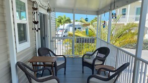 A covered porch with four wicker chairs and a table, overlooking a street with palm trees and a white van. - Relaxing  Home in gated community (Cudjoe Key)