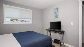 A bedroom with a bed, a TV on a stand, a window with blinds, and a wall with a floral print.