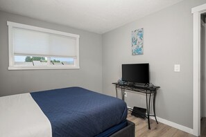 A bedroom with a bed, a TV on a stand, a window with blinds, and a wall with a floral print. - Updated Upstairs 2 Bedroom Apartment - 2 min to Browns Park (Spokane Valley)