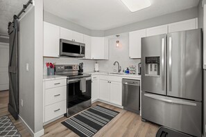 Una cocina moderna con armarios blancos, electrodomésticos de acero inoxidable, microondas, horno, lavavajillas y refrigerador.