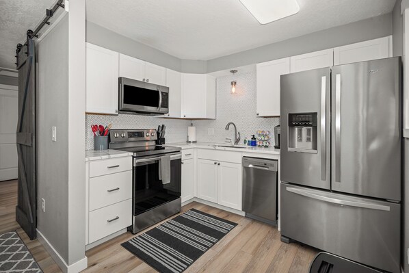 A modern kitchen with white cabinetry, stainless steel appliances, a microwave, oven, dishwasher, and a refrigerator.