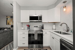 A compact kitchen with white cabinetry, a built-in microwave, a stainless steel oven, and a modern sink. - Updated Upstairs 2 Bedroom Apartment - 2 min to Browns Park (Spokane Valley)