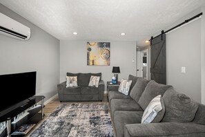A living room with a flat-screen TV, two grey sofas, a patterned rug, and a wall-mounted painting. - Updated Upstairs 2 Bedroom Apartment - 2 min to Browns Park (Spokane Valley)