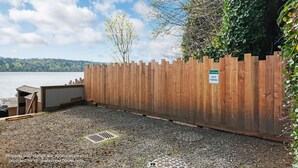 Ein Holzzaun mit einem 'Welcome'-Schild und einem Schild für 'Besucherparkplätze', ein Kiesplatz und Blick auf einen See.