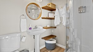 Ein modernes Badezimmer mit Waschbecken, Spiegel, Handtuchhalter, Dusche und Ablageflächen.