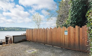 Una cerca de madera con un letrero que dice 'Welcome' y otro que indica 'Guest Parking', un área de grava y vista a un lago.