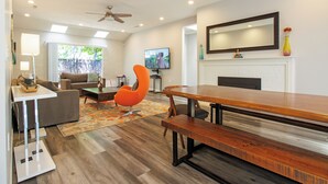 A modern living room with a wooden dining table, a sofa, a unique orange chair, and a fireplace.