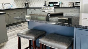 A modern kitchen with grey cabinets, a built-in oven, microwave, and a large island with bar stools.