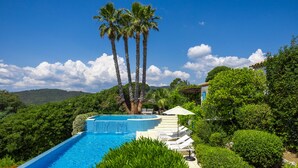 A swimming pool with a curved edge, surrounded by lush greenery and palm trees. - Golfvilla Riviera - luxury villa in the Golfe de Saint Tropez (Grimaud)