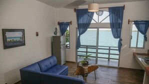 A room with a blue sofa, a small table with a plant, and a view of the sea through large windows with blue curtains. - Seven Blue House Village & Lodge (Bacalar)