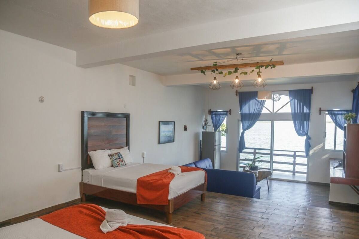 Ein Hotelzimmer mit zwei Betten, Holzboden, einem großen Fenster mit Vorhängen und Meerblick.
