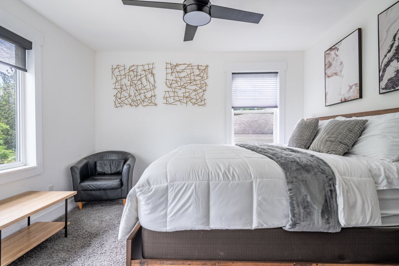 A bedroom with a bed, a chair, a desk, and artwork on the walls.