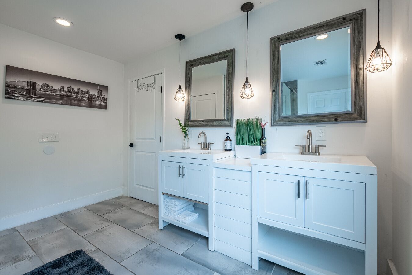 Un baño moderno con dos lavamanos, espejos grandes e iluminación colgante.