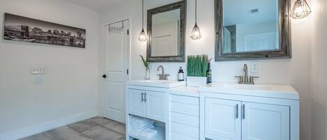 Un baño moderno con dos lavamanos, espejos grandes e iluminación colgante.