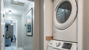 A laundry room with a front-loading washer and dryer, a hallway leading to a living area, and a ceiling with recessed lighting. - Top Level- Atlanta MBS Apartment w/ Private Hot tub (Atlanta)